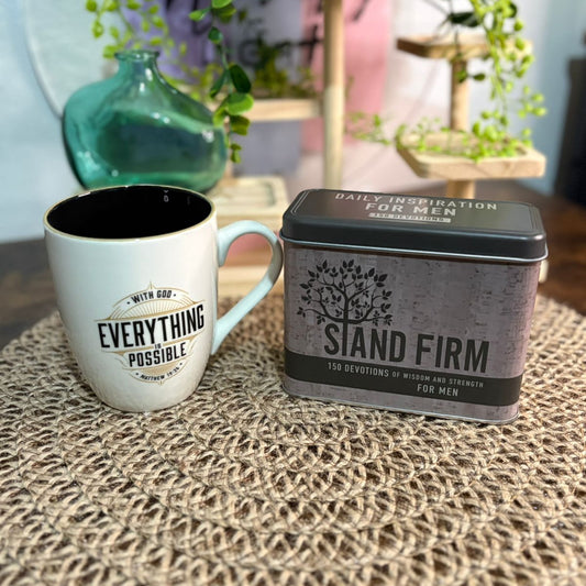 Mug with motivational quote and a tin box labeled 'Stand Firm' on a textured surface.